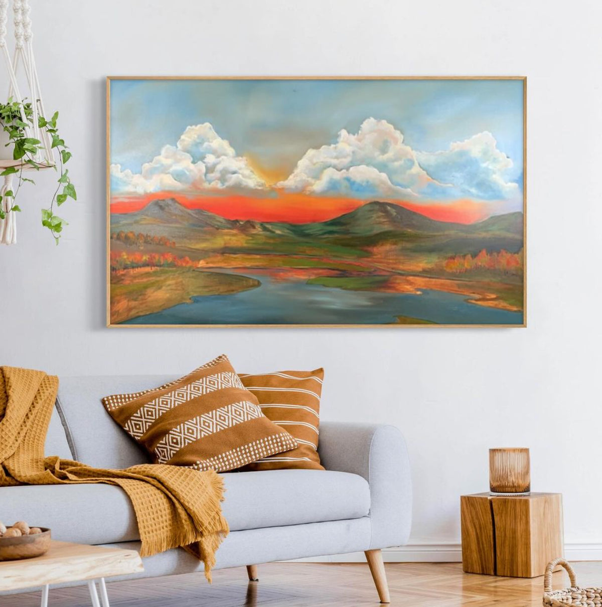 Framed painting of clouds, mountains, and a river above a sofa